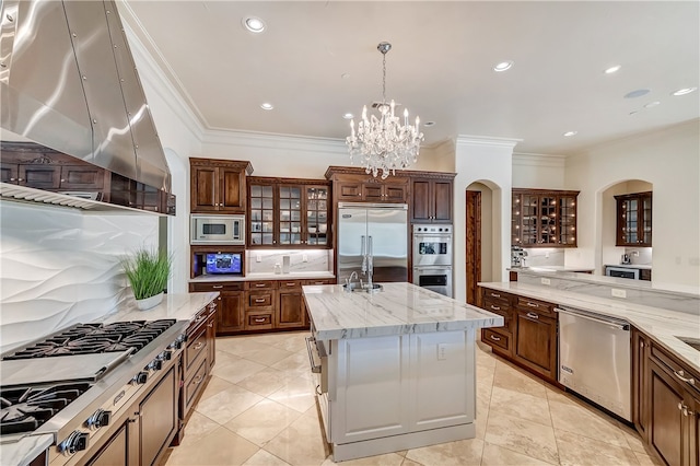 kitchen with a chandelier, light tile patterned floors, an island with sink, island exhaust hood, and built in appliances