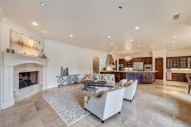 living room with an inviting chandelier, sink, light tile patterned floors, a tiled fireplace, and ornamental molding