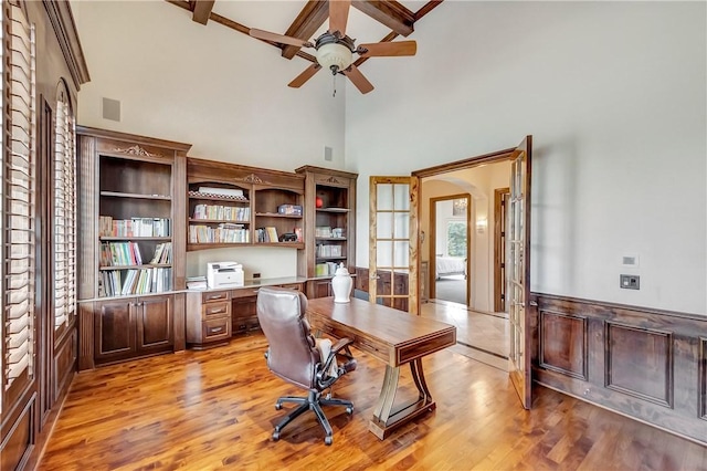 office space featuring light wood-style floors, built in desk, a ceiling fan, and wainscoting