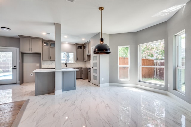 kitchen featuring a kitchen island, baseboards, marble finish floor, hanging light fixtures, and light countertops