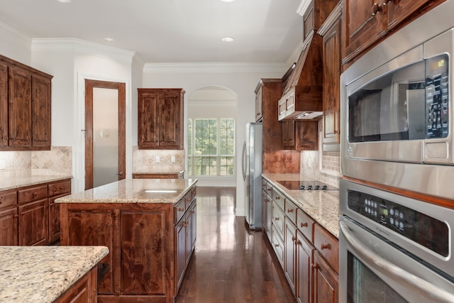 kitchen with light stone countertops, a center island, crown molding, backsplash, and appliances with stainless steel finishes