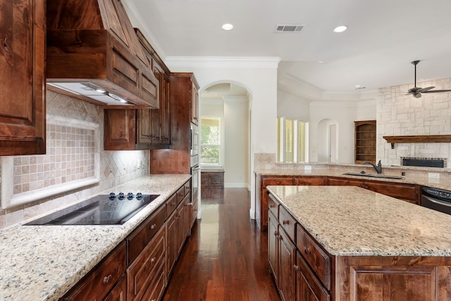 kitchen featuring light stone counters, a center island, black electric cooktop, backsplash, and sink