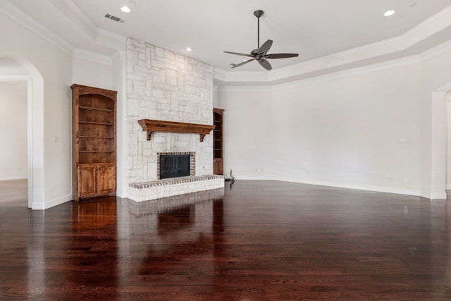 unfurnished living room with a stone fireplace, a raised ceiling, ceiling fan, ornamental molding, and dark hardwood / wood-style floors