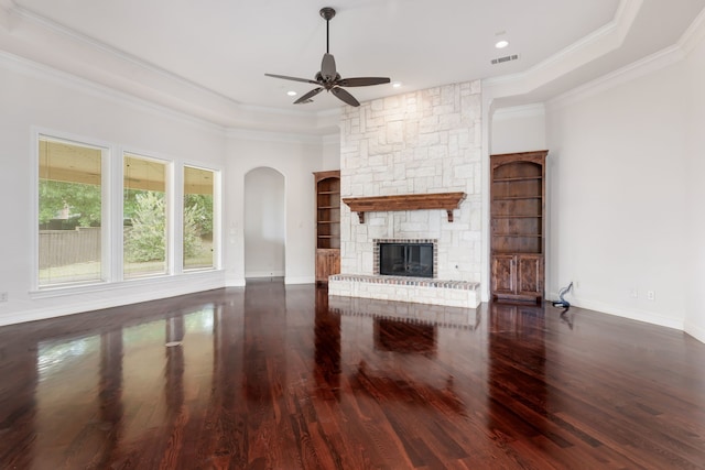 unfurnished living room with ceiling fan, a stone fireplace, a raised ceiling, and built in shelves