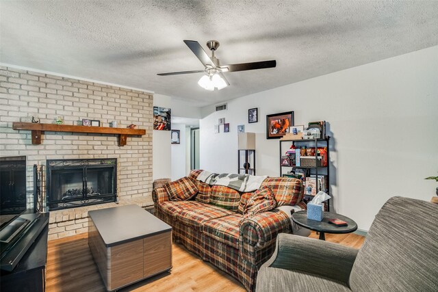 living room with a fireplace, light hardwood / wood-style floors, a textured ceiling, brick wall, and ceiling fan