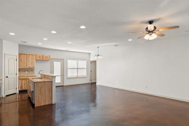 kitchen with light brown cabinetry, hanging light fixtures, ceiling fan with notable chandelier, sink, and a kitchen island with sink