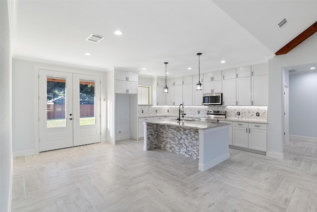 kitchen featuring light stone countertops, appliances with stainless steel finishes, white cabinetry, hanging light fixtures, and a center island with sink