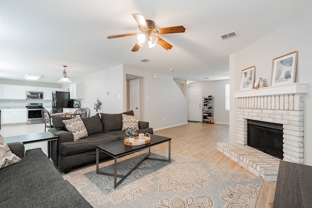 living room with ceiling fan, light hardwood / wood-style flooring, and a brick fireplace