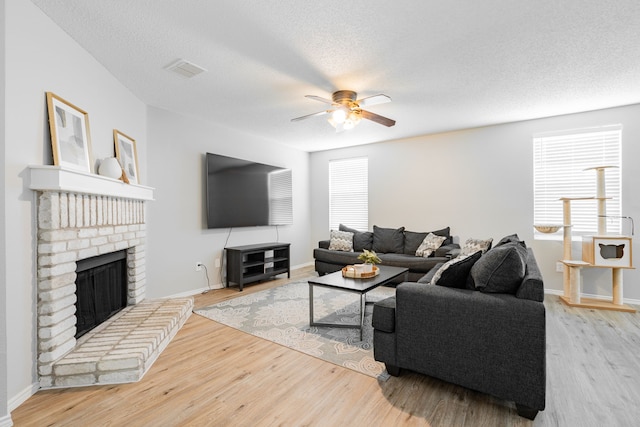 living room featuring a fireplace, a textured ceiling, light hardwood / wood-style flooring, and ceiling fan