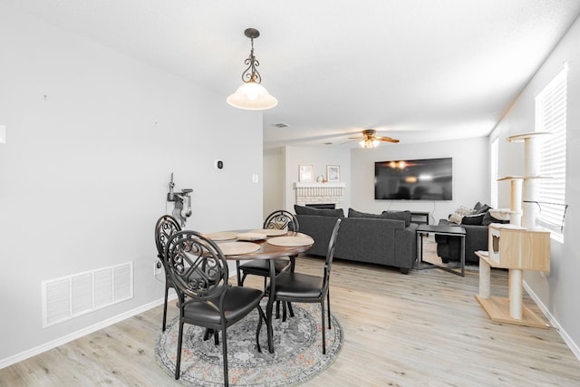 dining area featuring light hardwood / wood-style flooring, a brick fireplace, and ceiling fan