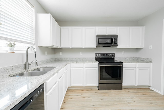 kitchen with stainless steel appliances, white cabinets, sink, light stone countertops, and light hardwood / wood-style flooring