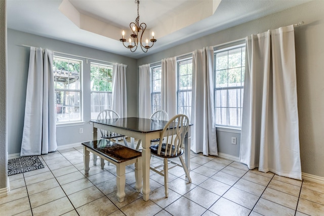 dining area with light tile patterned floors, a wealth of natural light, a tray ceiling, and a chandelier