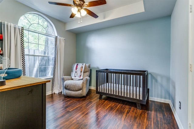 bedroom featuring a crib, dark wood-type flooring, and ceiling fan