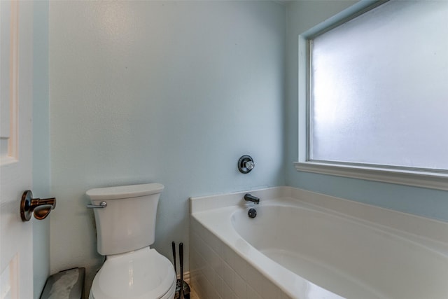 bathroom with tiled bath, plenty of natural light, and toilet