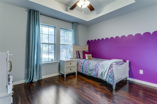 bedroom with dark hardwood / wood-style floors, a tray ceiling, and ceiling fan