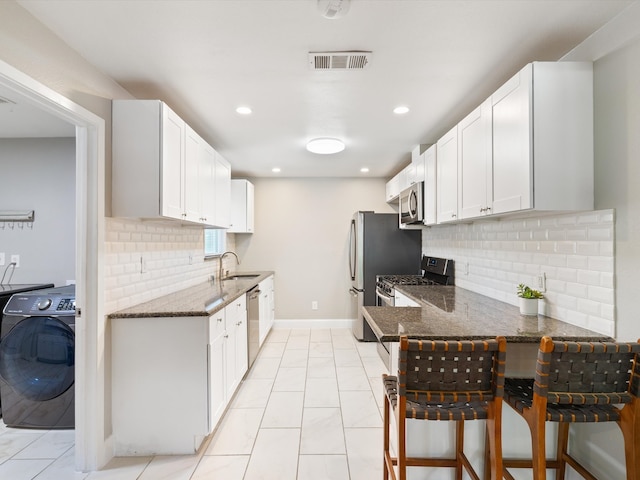 kitchen with stainless steel appliances, white cabinets, a breakfast bar area, washer / clothes dryer, and backsplash