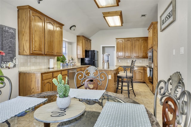 kitchen featuring tasteful backsplash, vaulted ceiling, appliances with stainless steel finishes, and a breakfast bar area