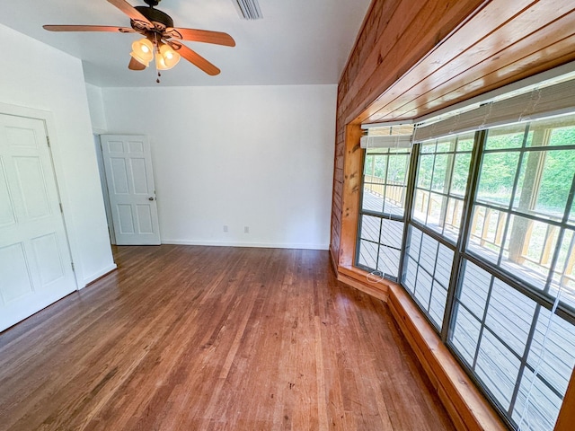 empty room with ceiling fan, wood walls, and hardwood / wood-style flooring