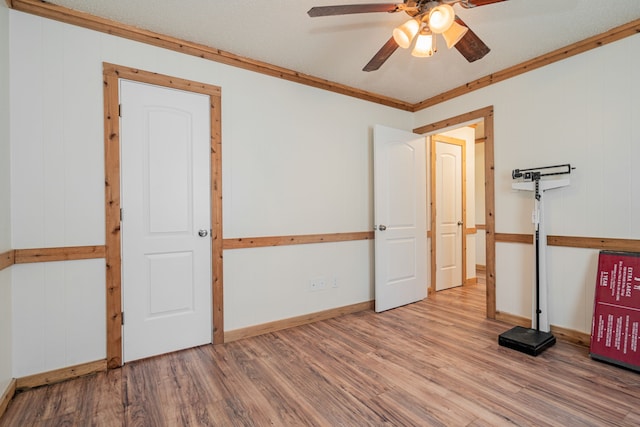 empty room featuring wooden walls, wood-type flooring, ornamental molding, and ceiling fan