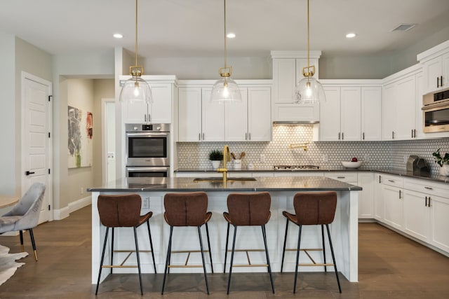 kitchen with sink, an island with sink, decorative light fixtures, and appliances with stainless steel finishes