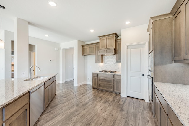 kitchen with light stone counters, hanging light fixtures, stainless steel appliances, and sink