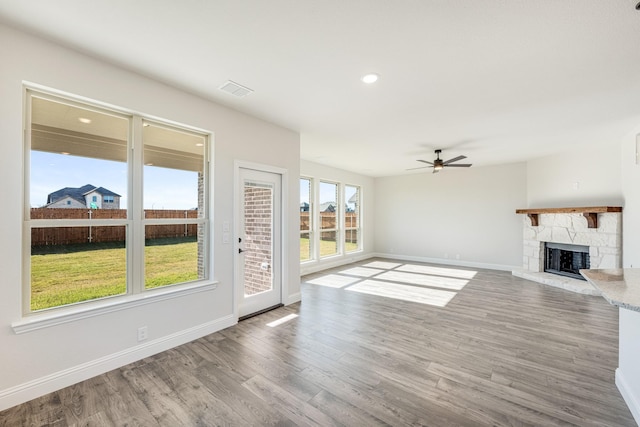 unfurnished living room featuring ceiling fan, a stone fireplace, and wood-type flooring