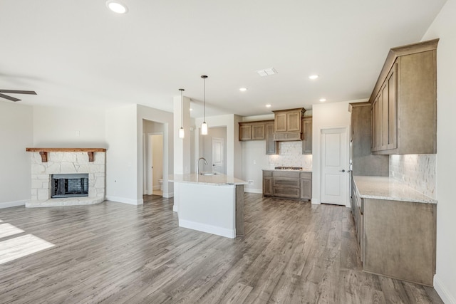 kitchen with a center island with sink, sink, light stone countertops, and backsplash