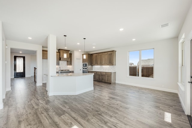 kitchen featuring hanging light fixtures, decorative backsplash, light stone countertops, built in microwave, and an island with sink