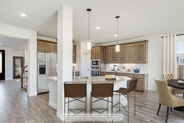 kitchen featuring light stone counters, a breakfast bar, stainless steel appliances, sink, and pendant lighting