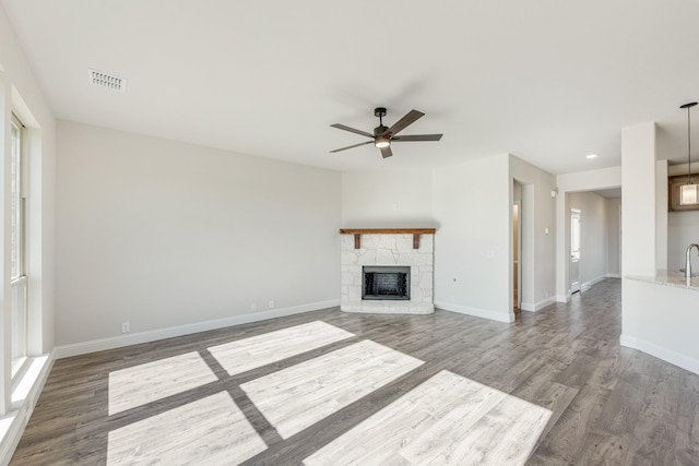 unfurnished living room featuring hardwood / wood-style flooring, ceiling fan, a stone fireplace, and sink