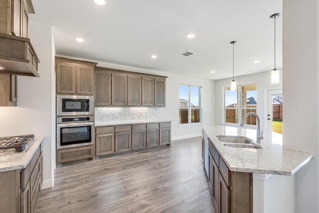 kitchen with sink, hanging light fixtures, backsplash, hardwood / wood-style floors, and appliances with stainless steel finishes