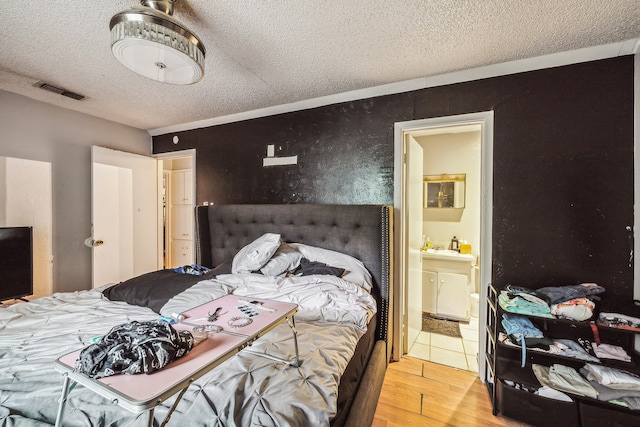 bedroom with ensuite bathroom, a textured ceiling, and light wood-type flooring