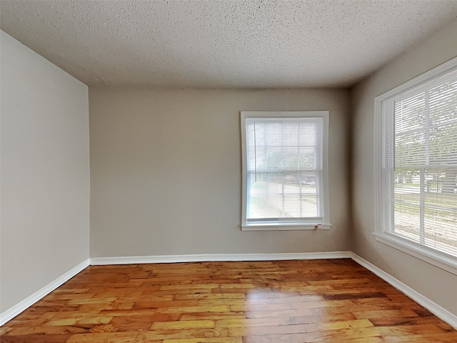 unfurnished room with light hardwood / wood-style floors, a textured ceiling, and plenty of natural light