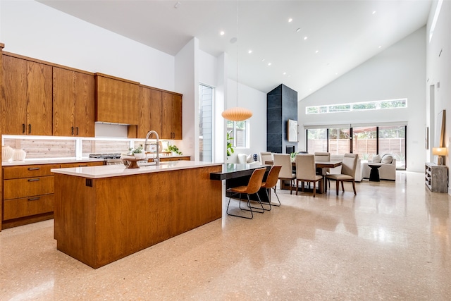 kitchen with pendant lighting, an island with sink, high vaulted ceiling, sink, and a breakfast bar