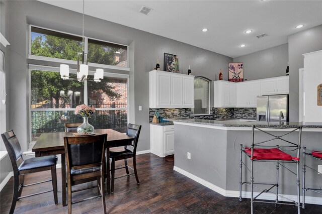 kitchen with white cabinets, pendant lighting, dark wood-type flooring, dark stone countertops, and an inviting chandelier