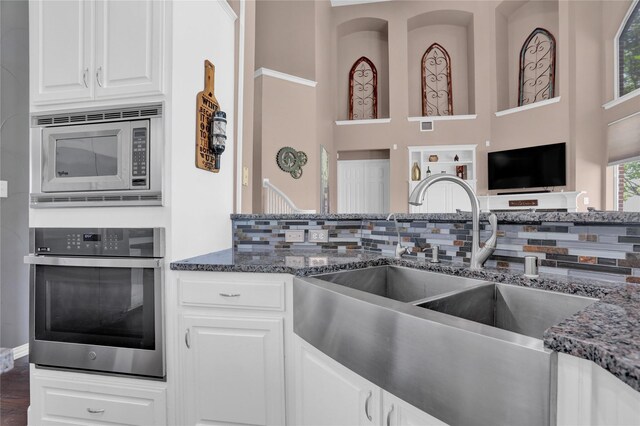 kitchen featuring tasteful backsplash, sink, white cabinetry, stainless steel appliances, and dark stone countertops