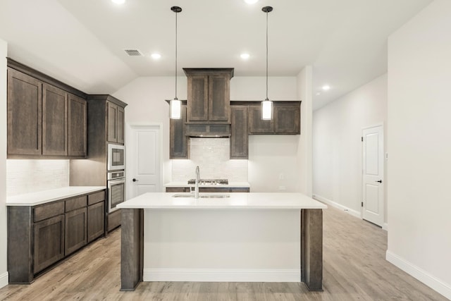 kitchen with decorative backsplash, stainless steel appliances, light hardwood / wood-style floors, and an island with sink