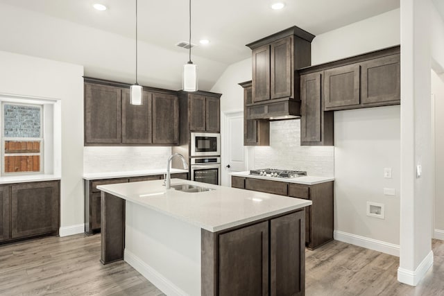 kitchen featuring backsplash, a center island with sink, hanging light fixtures, appliances with stainless steel finishes, and light hardwood / wood-style floors