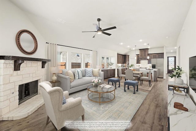 living room featuring a stone fireplace, plenty of natural light, light hardwood / wood-style floors, and lofted ceiling