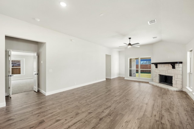 unfurnished living room with hardwood / wood-style flooring, ceiling fan, a stone fireplace, and lofted ceiling