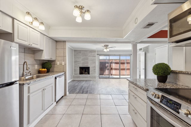 kitchen featuring stainless steel appliances, sink, white cabinets, a tile fireplace, and light tile patterned flooring