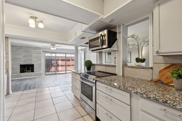 kitchen featuring light stone countertops, a tiled fireplace, light tile patterned floors, white cabinets, and appliances with stainless steel finishes