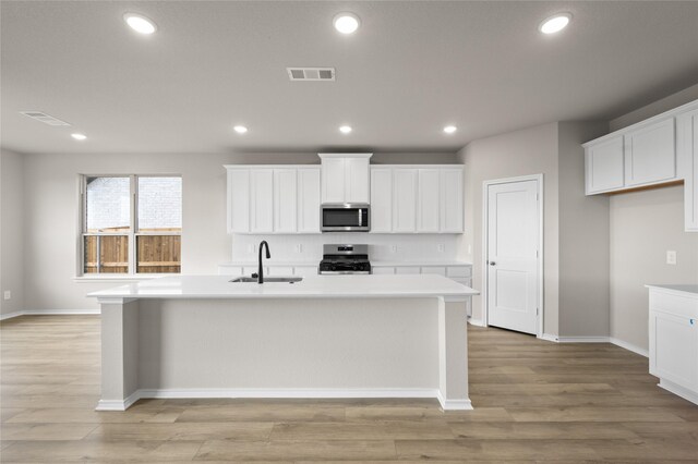 kitchen with a kitchen island with sink, appliances with stainless steel finishes, sink, and white cabinetry