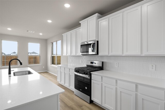 kitchen featuring white cabinetry, stainless steel appliances, decorative backsplash, light wood-type flooring, and sink