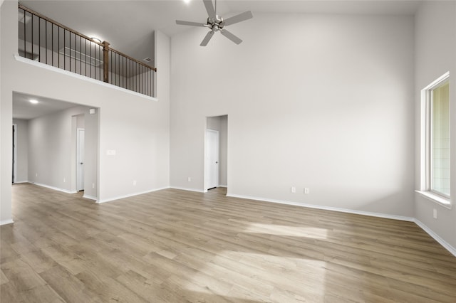 unfurnished living room with ceiling fan, light hardwood / wood-style floors, and a towering ceiling