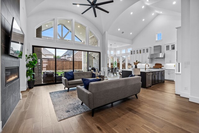 kitchen featuring built in appliances, an island with sink, wall chimney range hood, and high vaulted ceiling