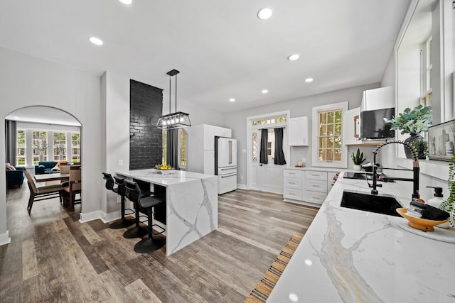 kitchen with pendant lighting, sink, a breakfast bar, light stone counters, and white cabinets