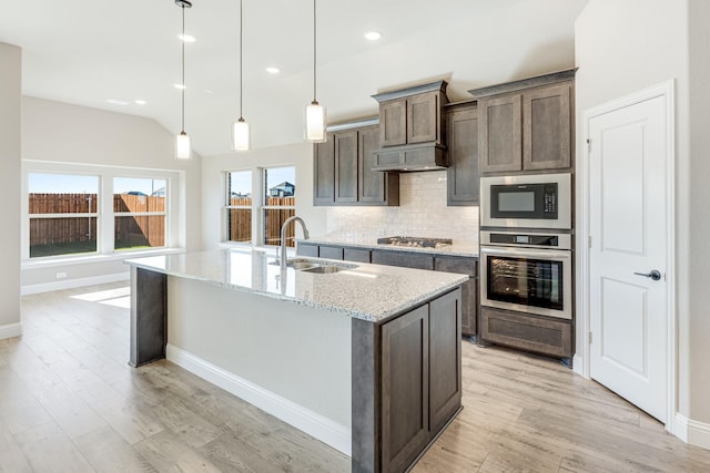 kitchen with sink, light stone countertops, an island with sink, decorative light fixtures, and stainless steel appliances