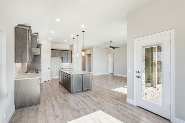 kitchen featuring tasteful backsplash, ceiling fan, decorative light fixtures, light hardwood / wood-style flooring, and an island with sink