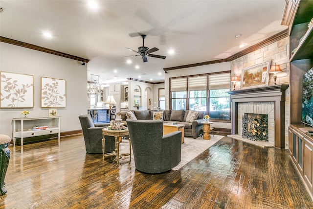 living room featuring ceiling fan with notable chandelier, hardwood / wood-style flooring, ornamental molding, and a fireplace